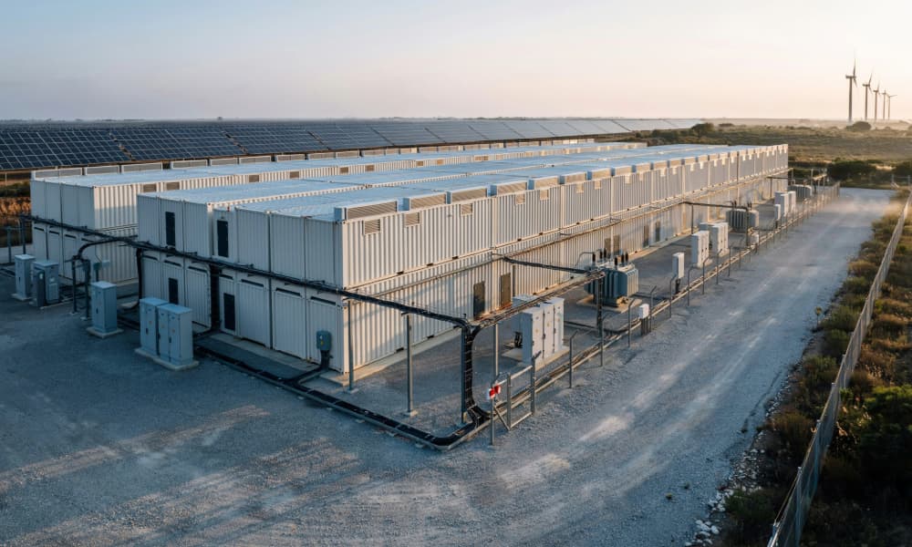 A battery storage facility beside solar panels and wind turbines
